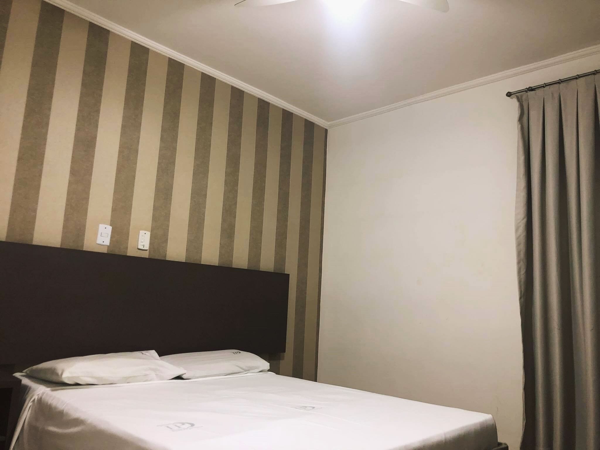 A hotel room with a striped wall, a bed with white bedding, and a dark headboard.