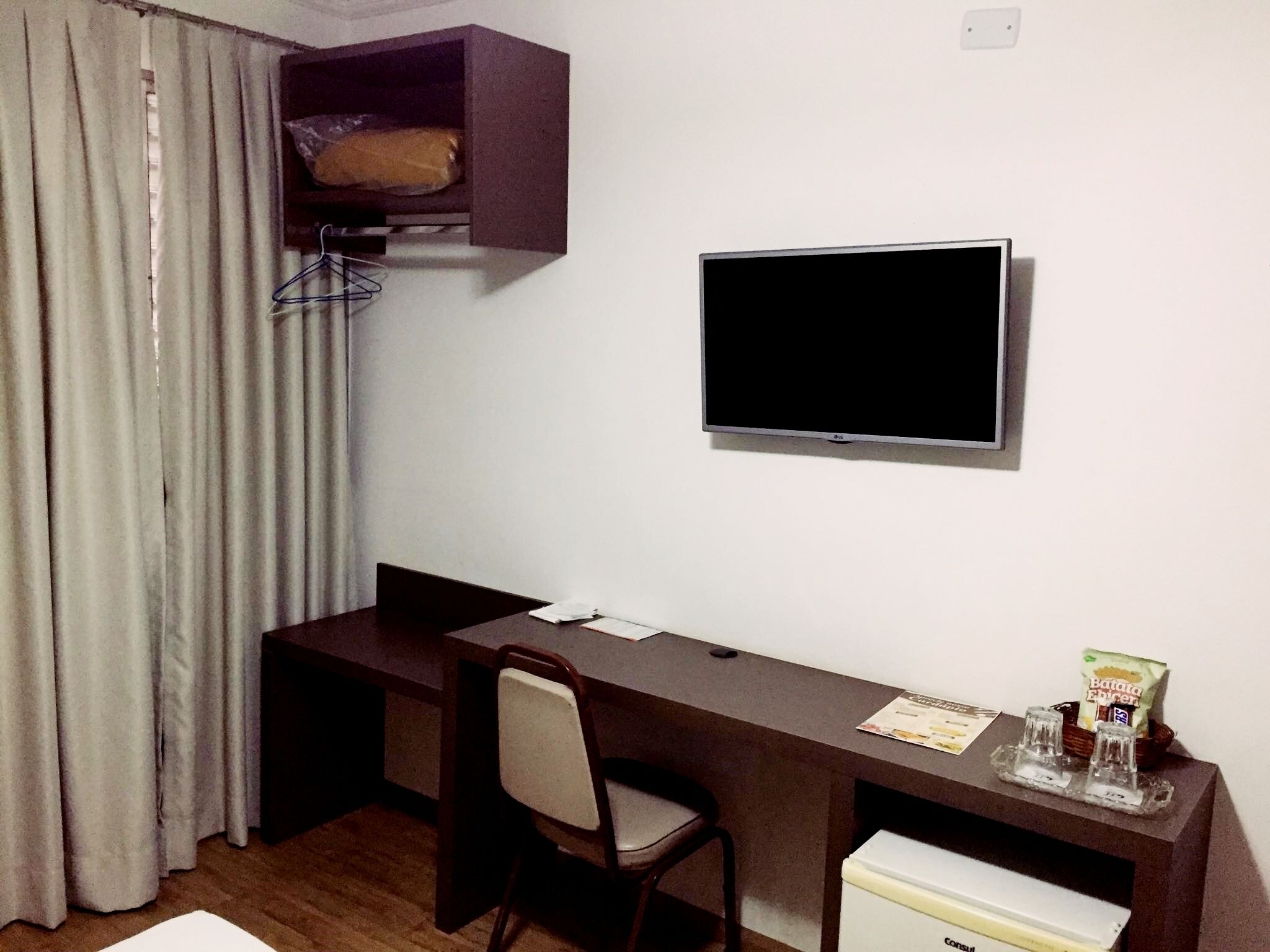 A hotel room with a desk, chair, television, and a small refrigerator.