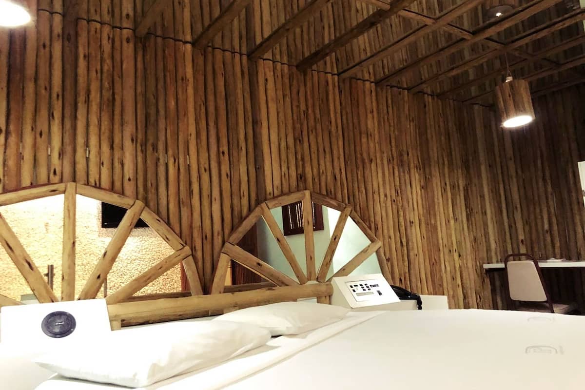 Ein Zimmer mit Holzboden und -wänden, einem Bett mit weißer Bettwäsche und einem kleinen Tisch mit Stuhl.