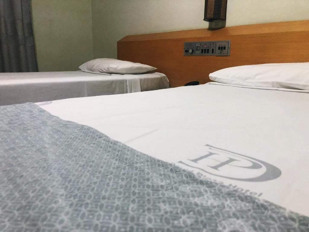 A hotel room with two single beds, a wooden headboard, and a control panel on the wall.
