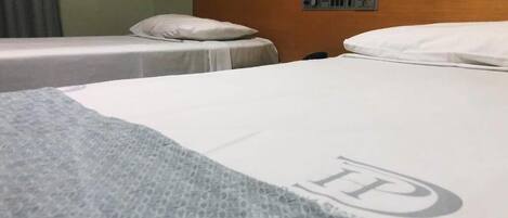 A hotel room with two single beds, a wooden headboard, and a control panel on the wall.
