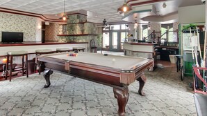 A pool table in a room with patterned carpet, a bar area, and a television. - Stone Waters Inn (Bellaire)