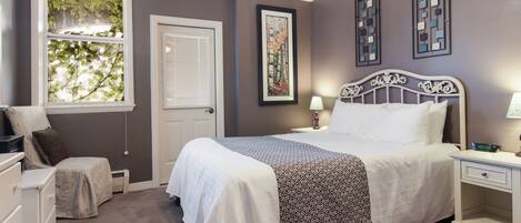 A bedroom with a bed, bedside tables, a dresser, a window with blinds, and a door.