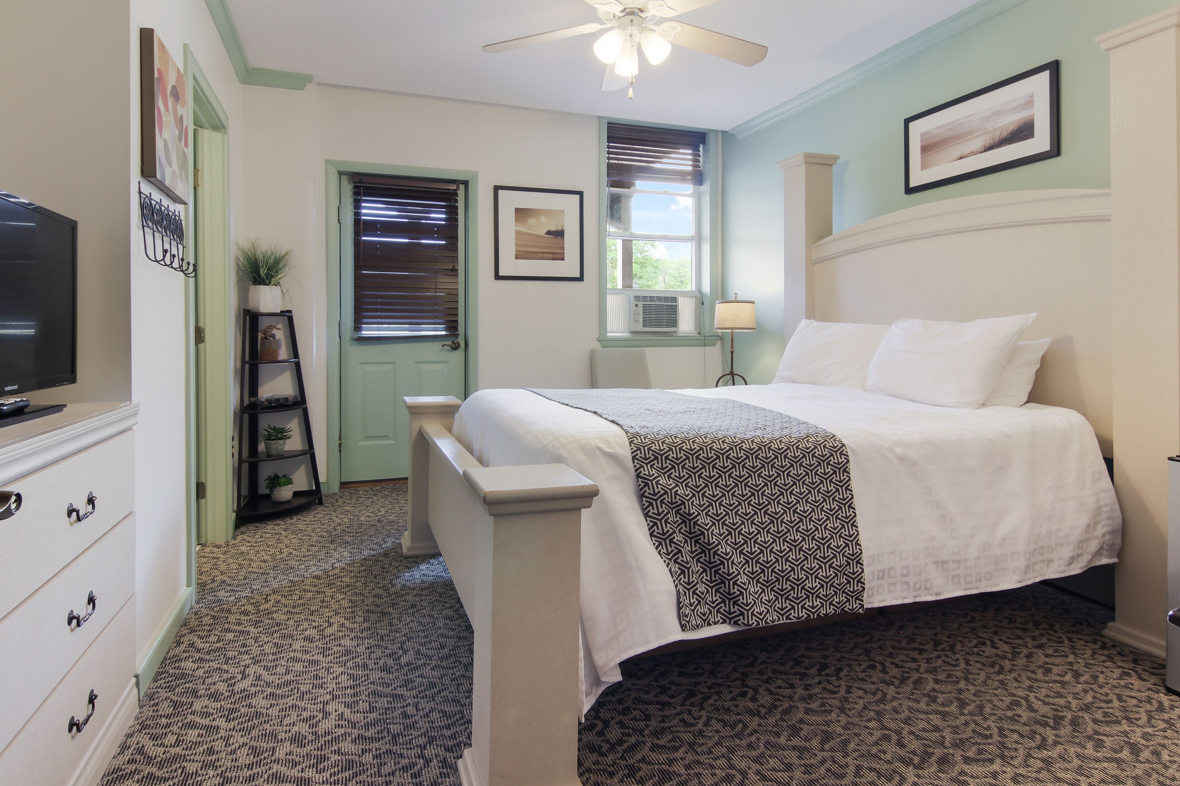 A bedroom with a bed, a dresser, a television, a ceiling fan, and a window with blinds.