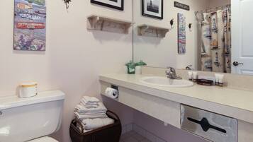 A bathroom with a toilet, sink, and mirror. There are towels stacked in a basket and a shower curtain with nautical designs.