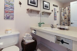 A bathroom with a toilet, sink, and mirror. There are towels stacked in a basket and a shower curtain with nautical designs.