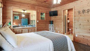 A wooden cabin room with a bed, a mirror, a television, and a small kitchenette. - Stone Waters Inn (Bellaire)