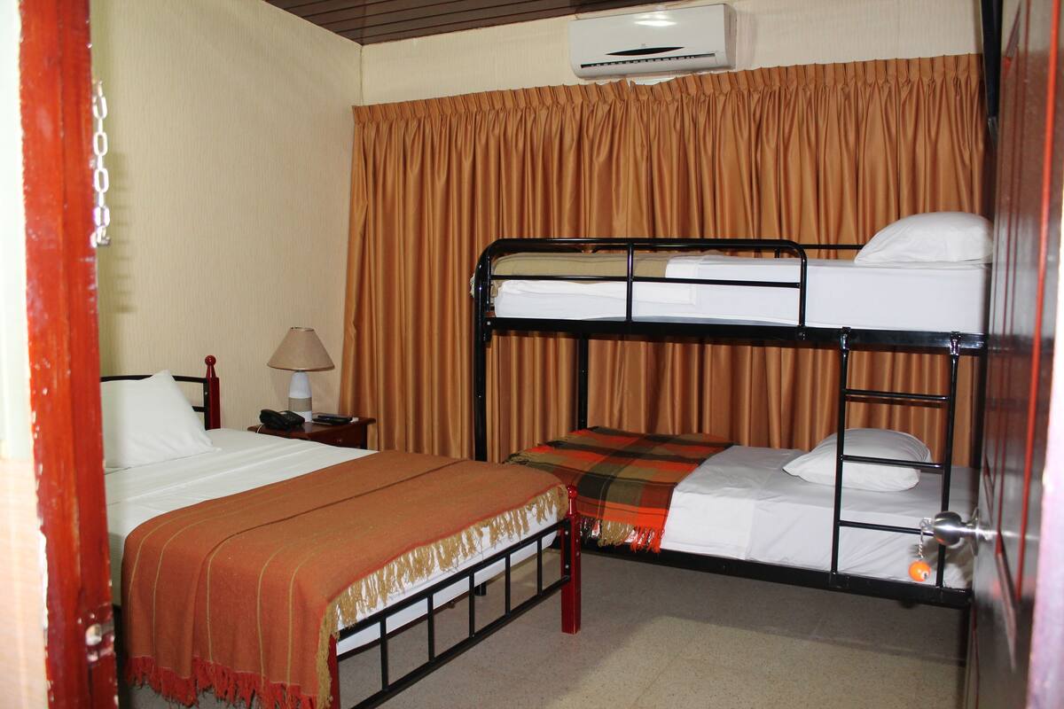 A hotel room with two beds, a lamp, and an air conditioning unit.