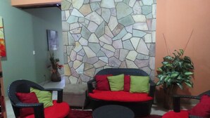 Un área de estar con sillones y otomanes de mimbre, una pared de piedra y una planta en maceta.