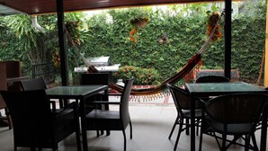 Un patio exterior con mesas y sillas, una hamaca y vistas a un jardín exuberante.