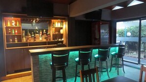 Una zona de bar con mostrador, taburetes y estantes llenos de botellas.