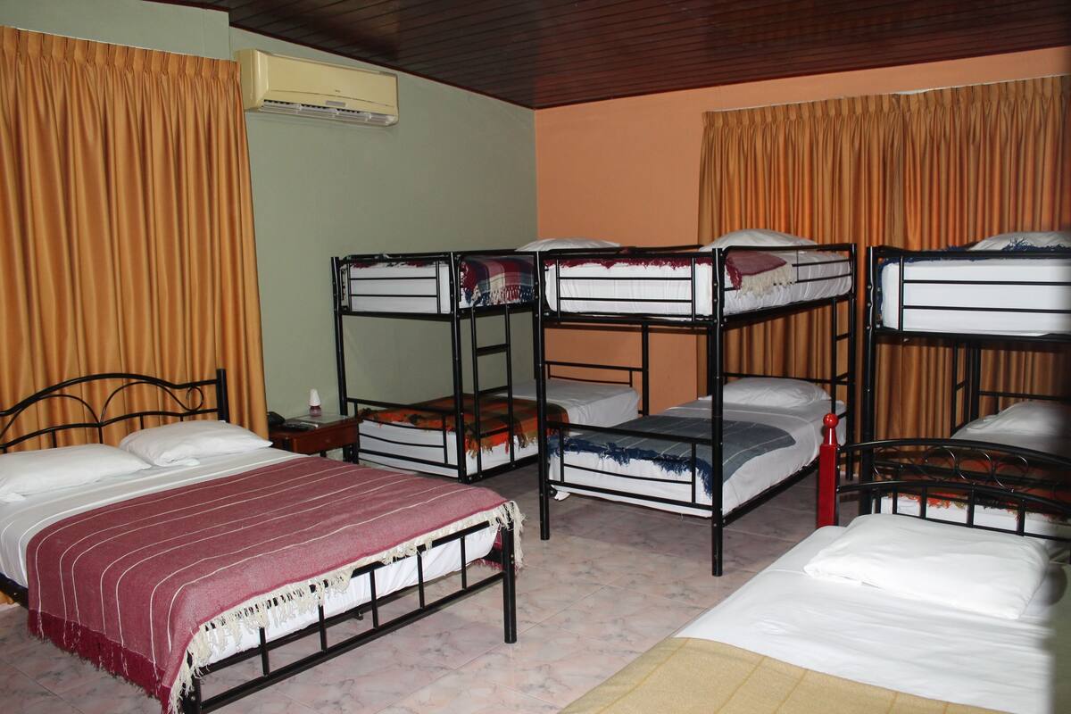 A dormitory room with bunk beds, a single bed, and an air conditioning unit on the wall.