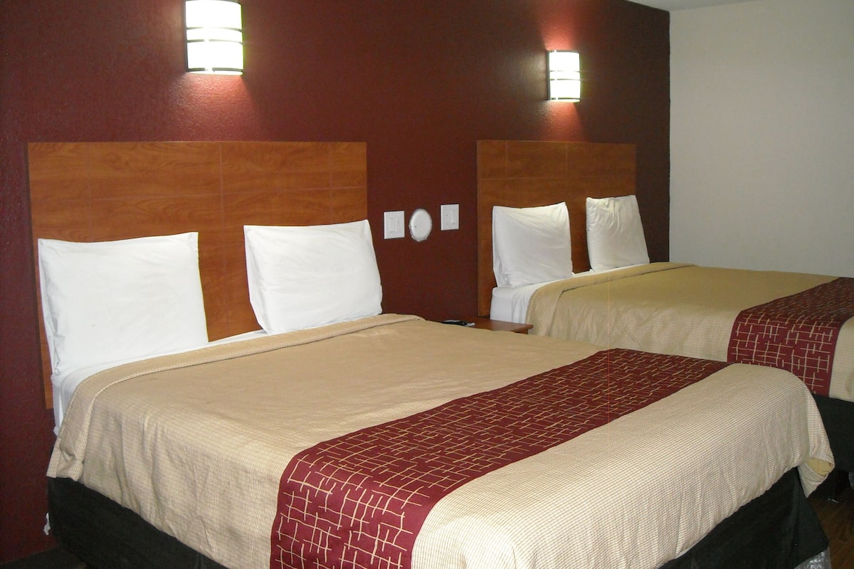 A hotel room with two beds, each with white pillows and beige bedding.