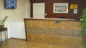 A reception area with a tiled floor, a reception desk, a potted plant, a framed picture, and a sign with room rules. - Bastrop Inn (Bastrop)