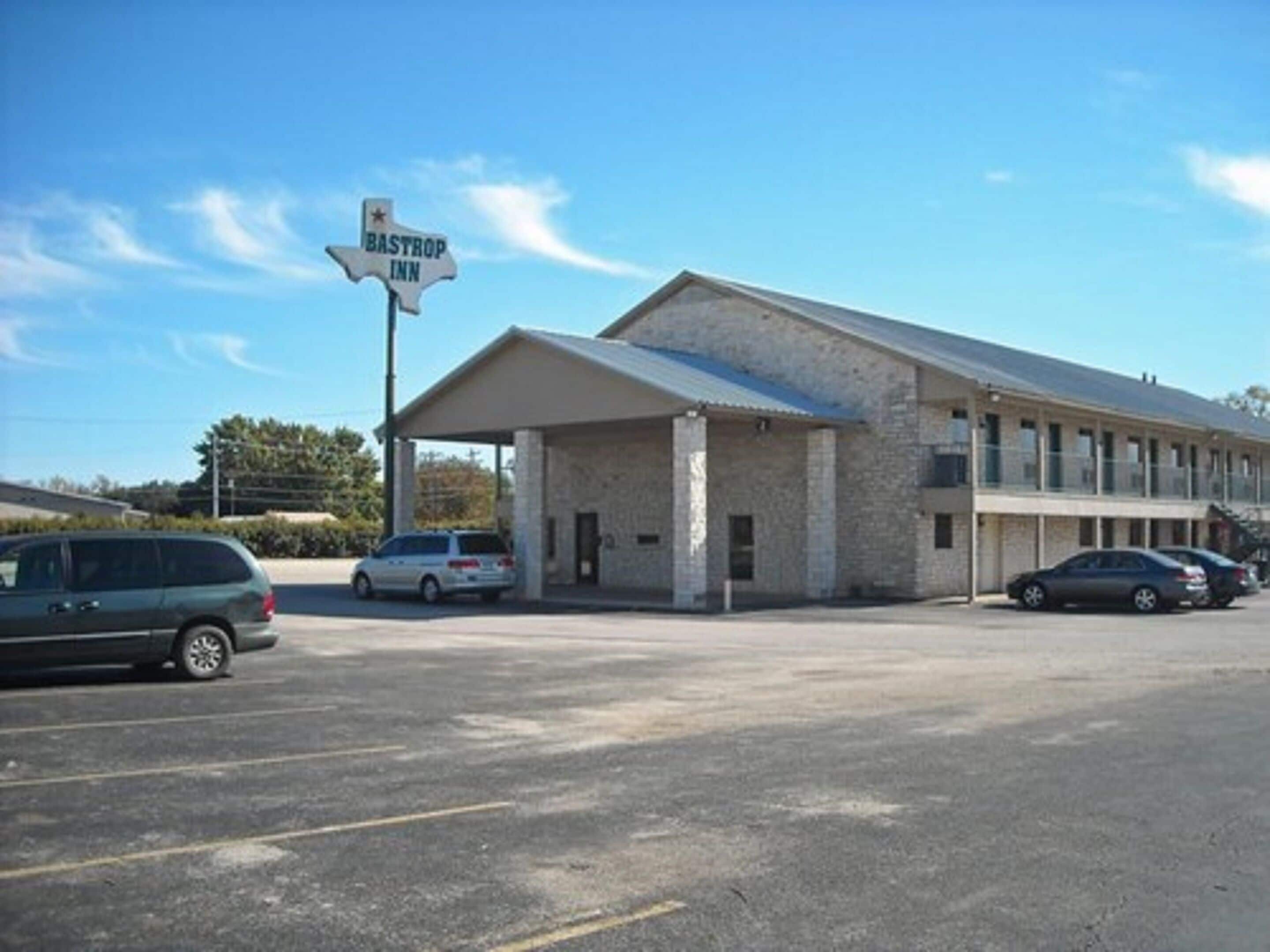 Un motel con zona de estacionamiento techada y un cartel que indica 'Bastrop Inn'.