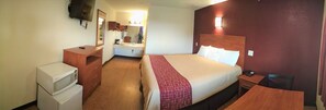 Habitación de hotel con cama, escritorio, silla, microondas, refrigerador, espejo y televisión.