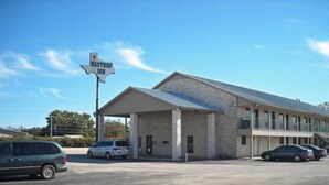 A motel with a large sign reading "Bastrop Inn" and a covered parking area with several cars. - Bastrop Inn (Bastrop)