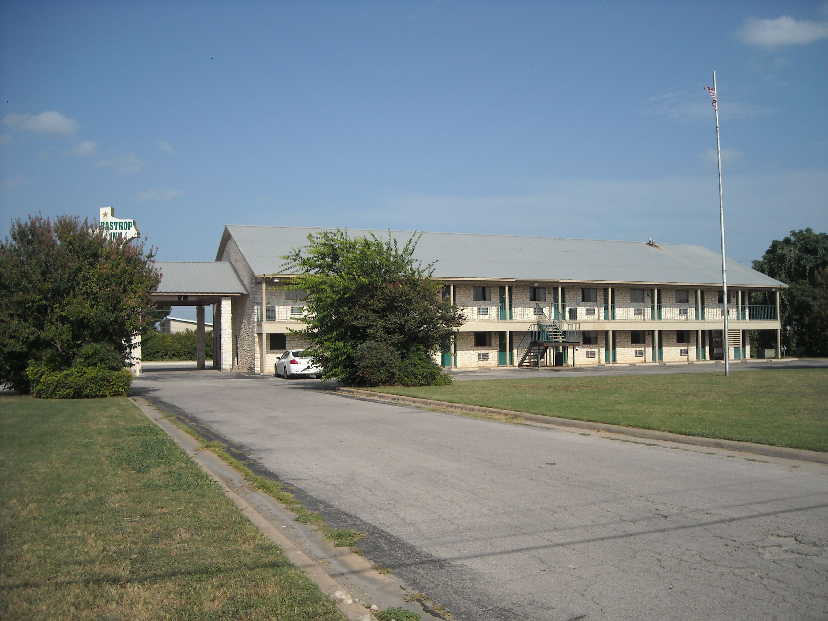 A two-story motel with a flat roof, a covered parking area, and a flagpole.