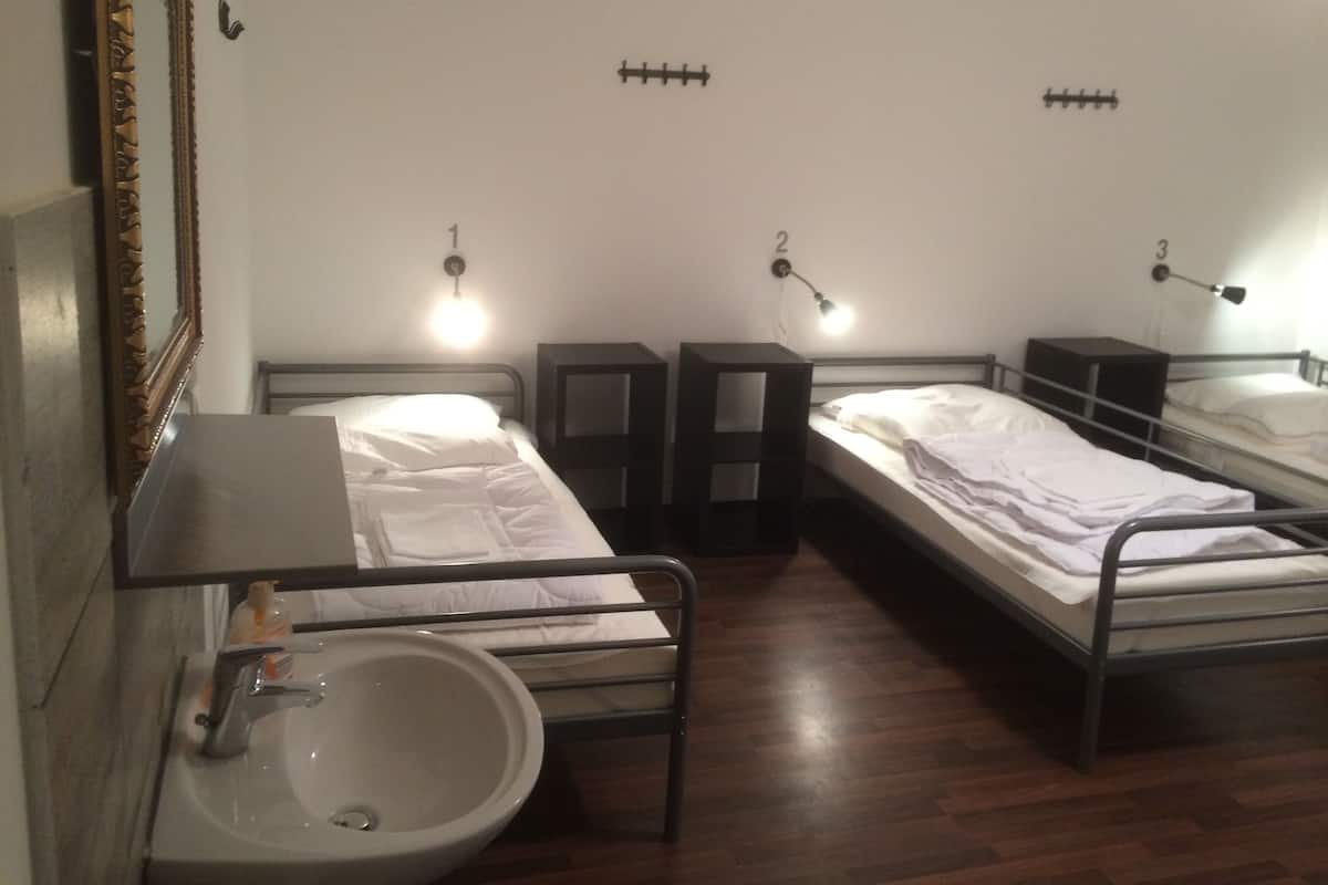 Ein Zimmer mit drei Einzelbetten, einem Waschbecken und einem Spiegel.