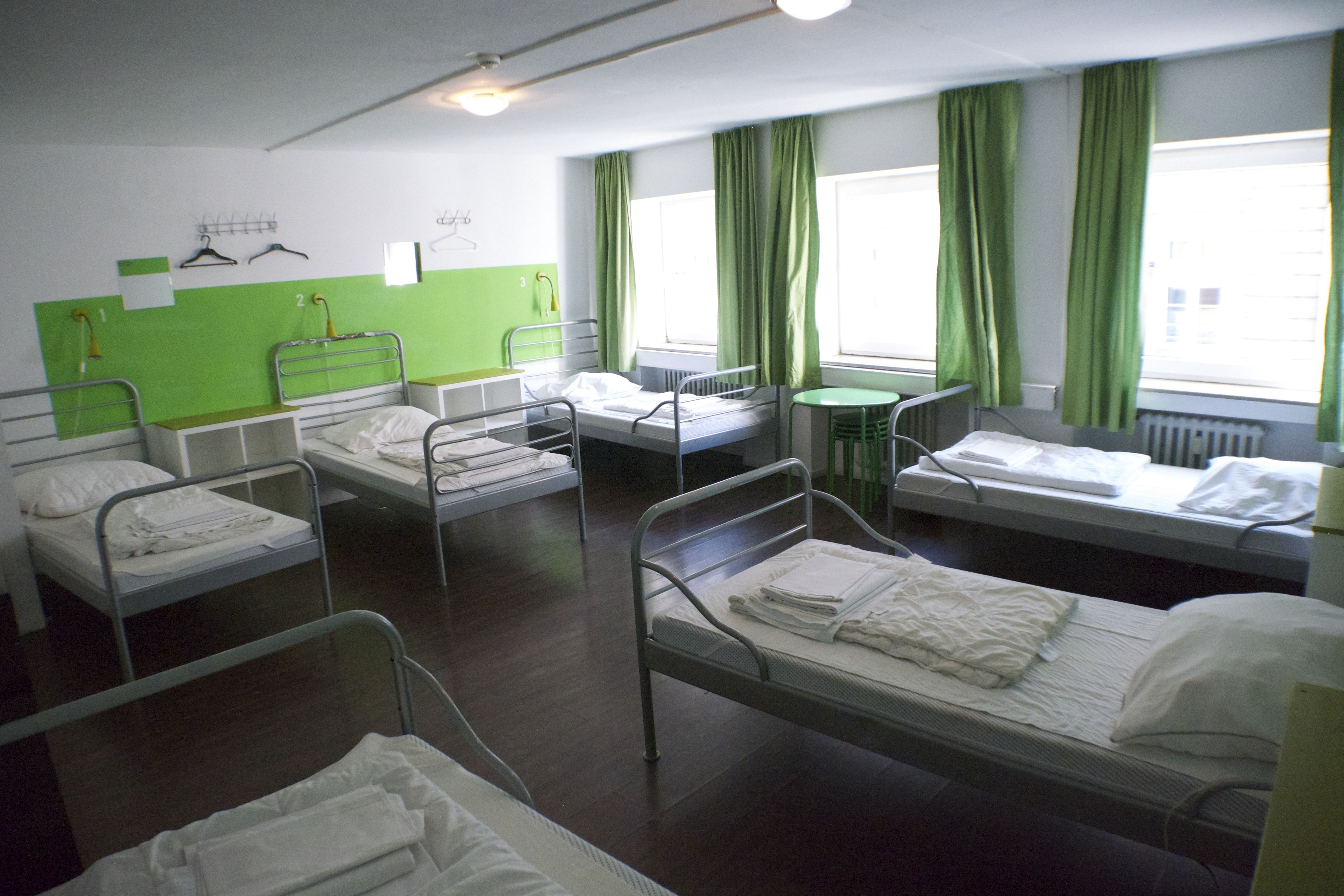 A hospital room with four beds, a small table, and green curtains.