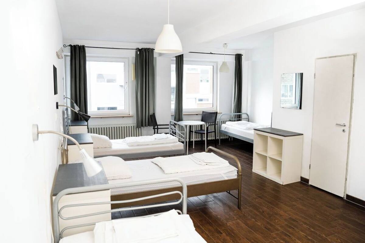 Ein Hotelzimmer mit zwei Einzelbetten, einem Schreibtisch, einem Stuhl, einem Heizkörper und einem Fenster mit Vorhängen.