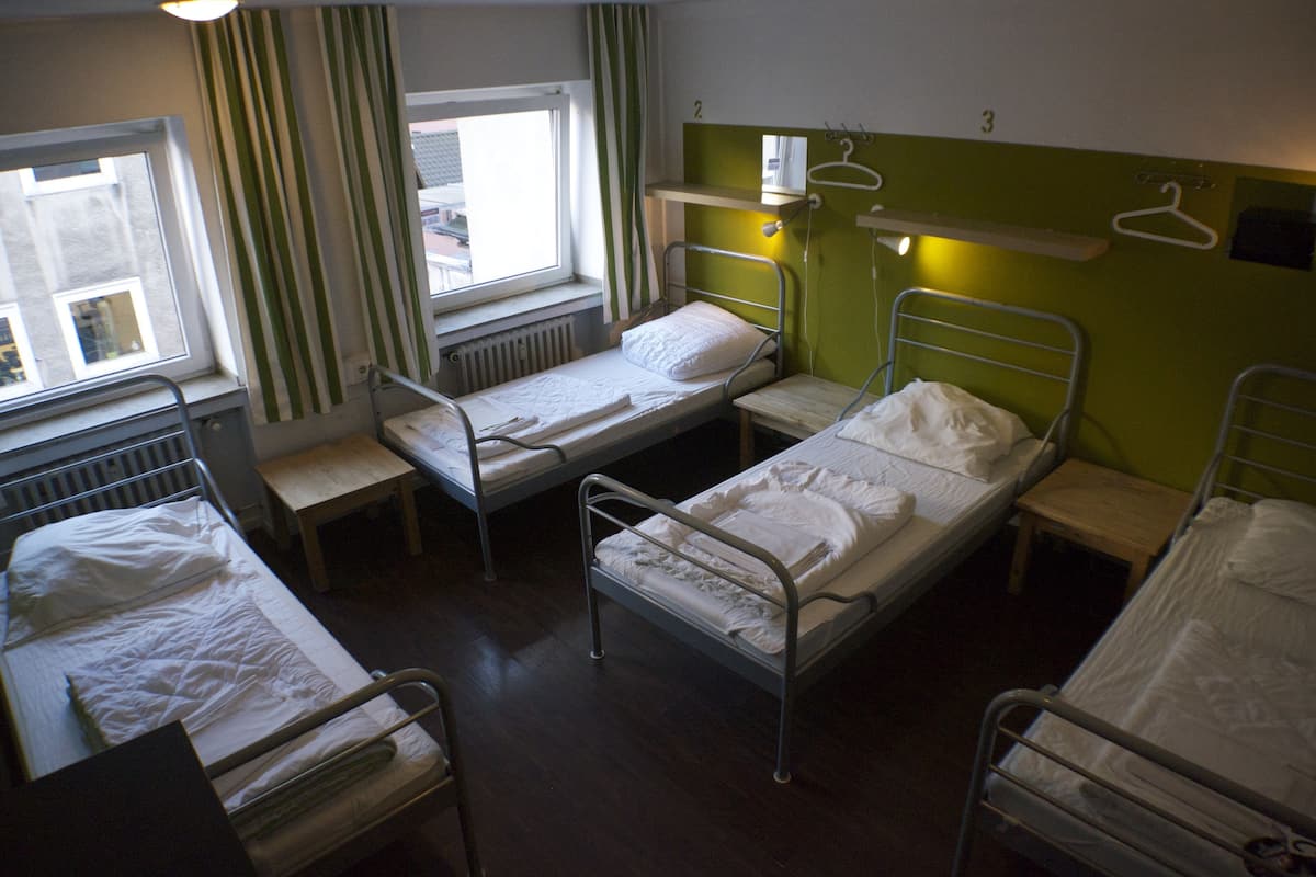 Ein Schlafsaalzimmer mit Etagenbetten, einem Fenster mit Vorhängen und einem kleinen Regal mit Spiegel und Kleiderhaken.