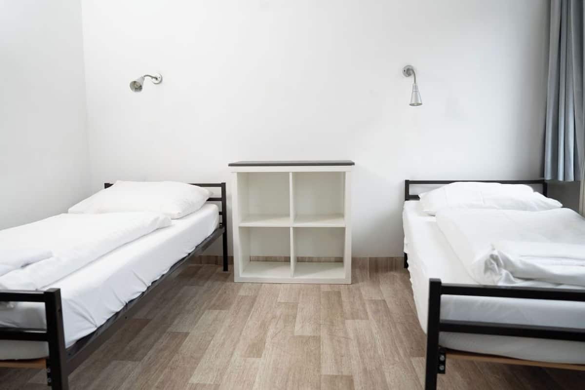 Ein Zimmer mit zwei Einzelbetten, einem weißen Kleiderschrank und einem Duschbereich.