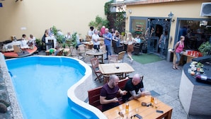 Un área junto a la piscina con mesas y sillas, un bote pequeño y un edificio con un letrero.