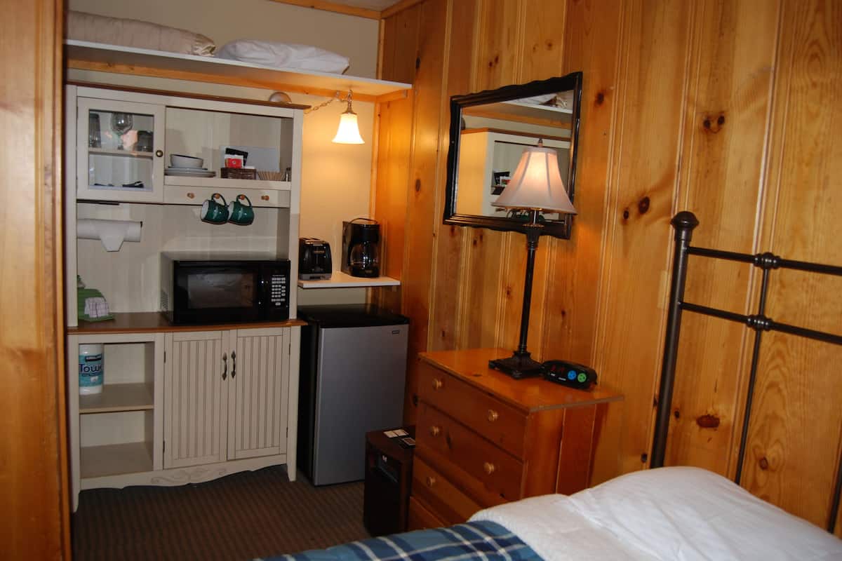 Quarto de hotel pequeno com cozinha compacta, uma cama, um espelho e uma luminária.