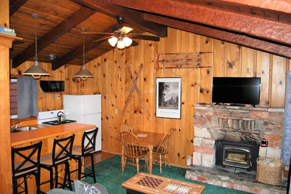 Interior de uma cabana de madeira com cozinha, sala de jantar e lareira.
