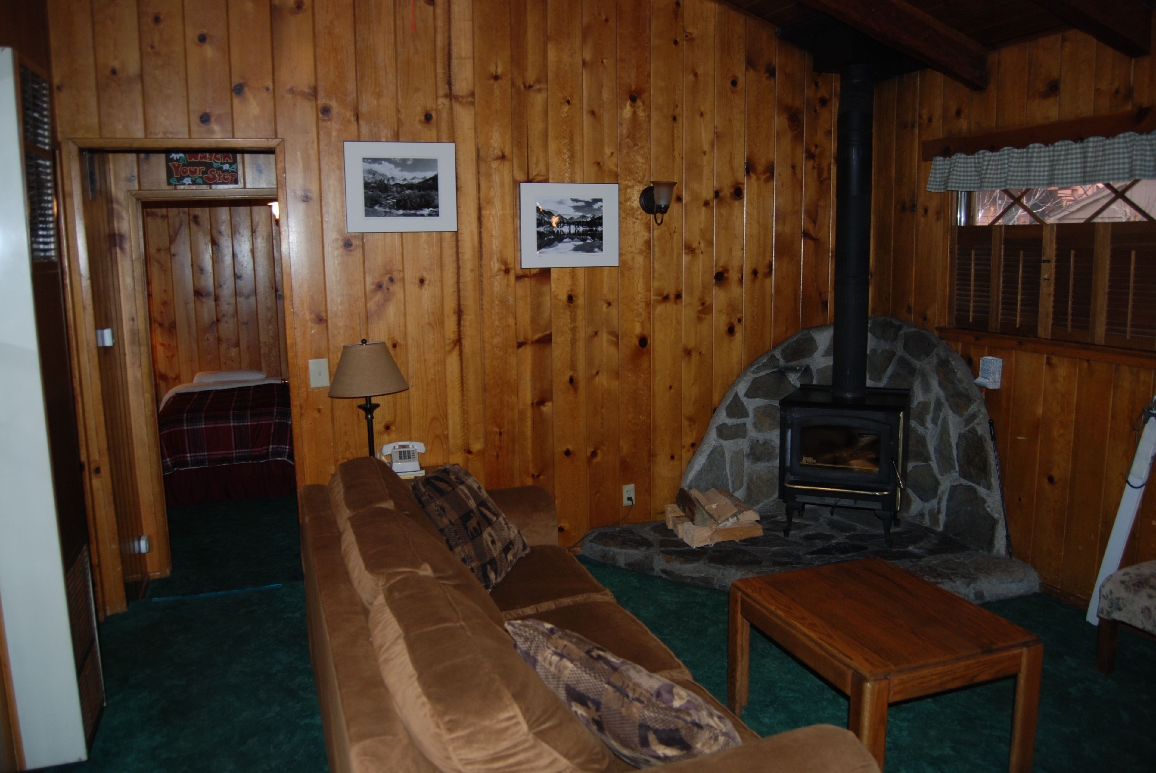 A cozy cabin interior with a stone fireplace, wooden walls, a brown sofa, and a small table.