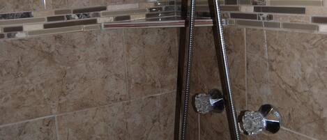 Eine Dusche mit Handbrause und fest installierter Duschbrause, beide mit Chromoberflächen, vor einer gefliesten Wand mit Marmormuster.