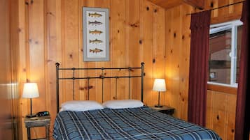 A wooden-paneled room with a bed, two bedside tables, lamps, and a framed fish illustration on the wall.