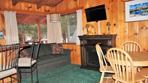 A cozy cabin interior with a fireplace, wooden walls, a television, and a dining area. - Edelweiss Lodge (Mammoth Lakes)