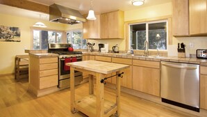 A modern kitchen with wooden cabinets, a stainless steel dishwasher, and a central island with a sink. - Edelweiss Lodge (Mammoth Lakes)