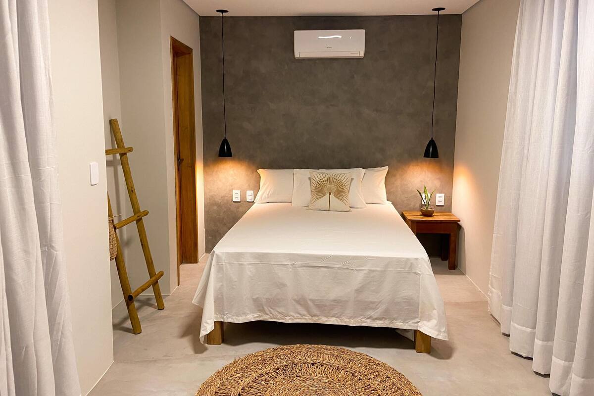Ein Schlafzimmer mit Bett, Nachttischlampen, einer Wand-Klimaanlage und einer Holzleiter.