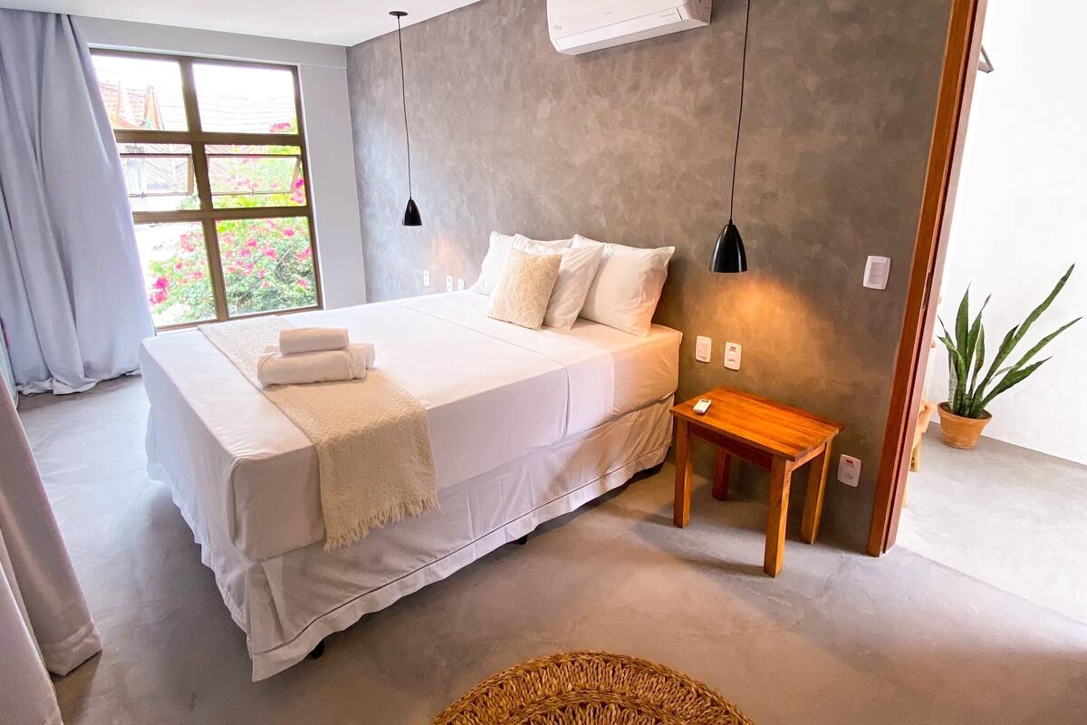 Ein modernes Schlafzimmer mit einem großen Bett, einem Nachttisch, einer kleinen Holzbank und einem Blumentopf.