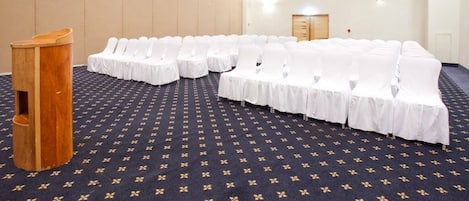 A conference room with rows of white-covered chairs and a wooden podium.