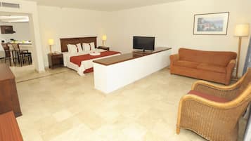Habitació d'hotel amb llit, televisió, sofà, zona de menjador i cadira de vimet.