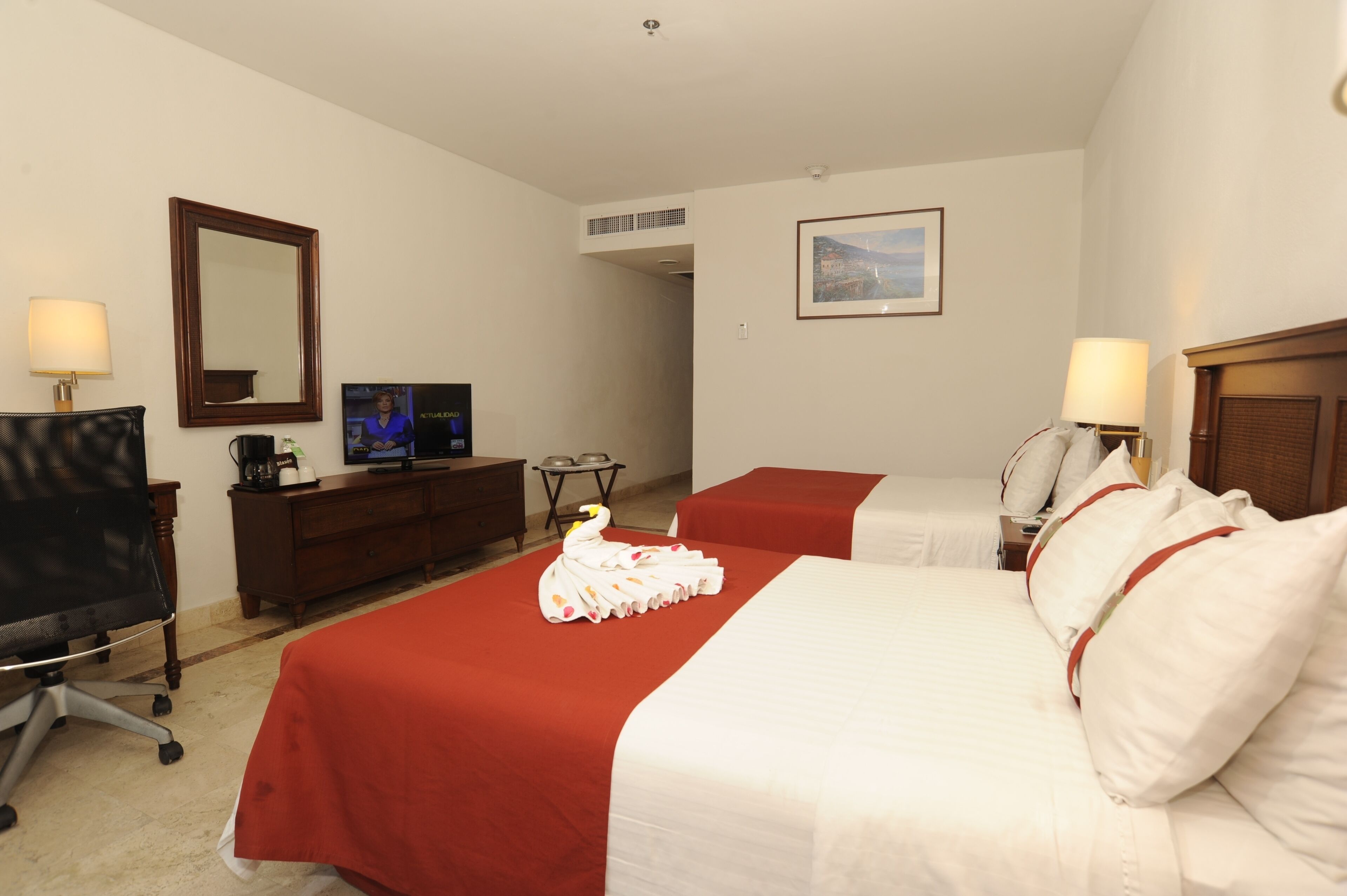 A hotel room with two beds, a desk, a chair, a television, and a framed picture on the wall.