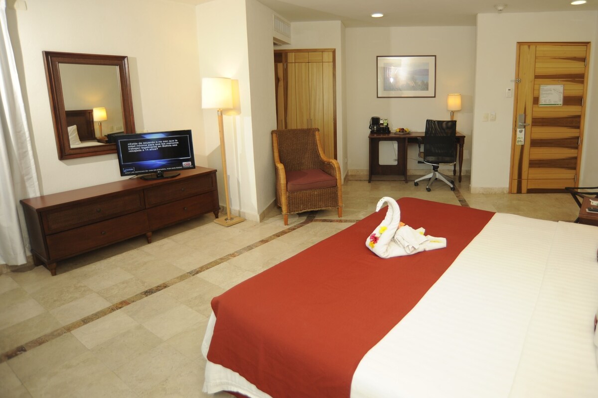 Una habitación de hotel con una cama, televisión, escritorio, silla y lámpara de escritorio.