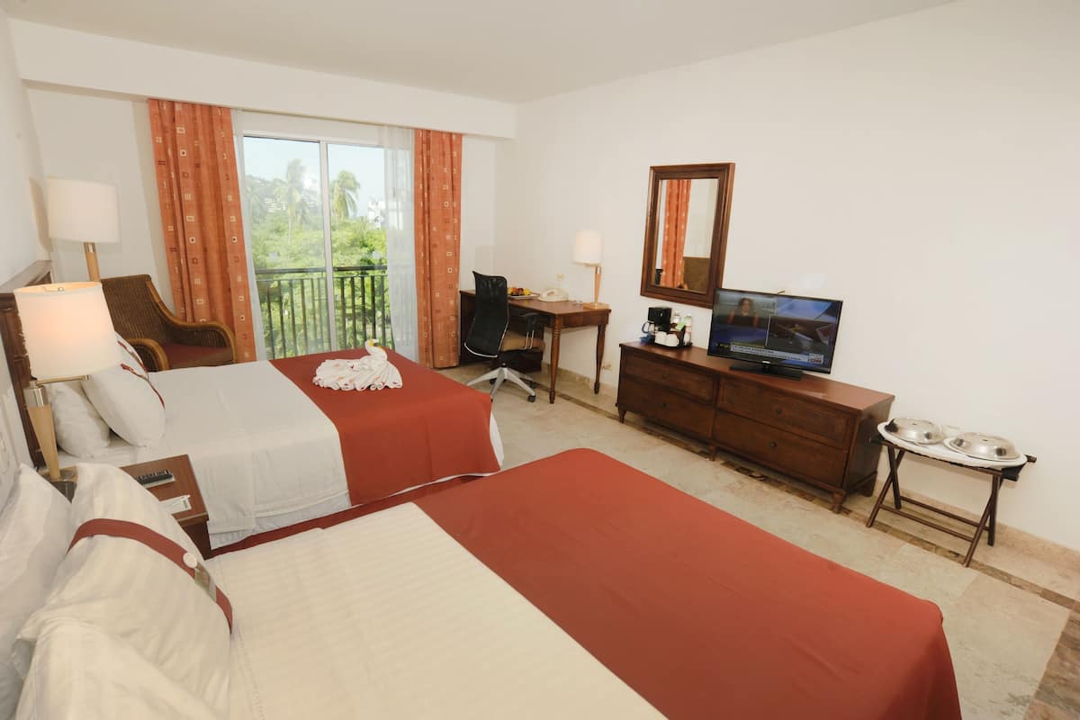 A hotel room with two beds, a desk, a television, and a balcony with curtains.