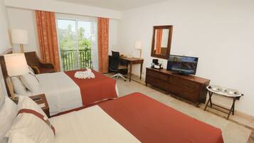 Quarto de hotel com duas camas, uma escrivaninha, televisão e varanda com cortinas.