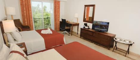 A hotel room with two beds, a desk, a television, and a balcony with curtains.