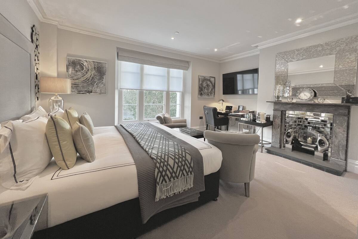 A modern bedroom with a large bed, a desk, and a fireplace.