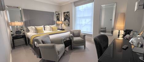 A hotel room with a large bed, two armchairs, a desk, and a large window.