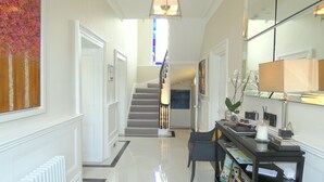 A hallway with a staircase, a black console table with various items, and a large mirror. - Tavistock House Hotel (Tavistock)