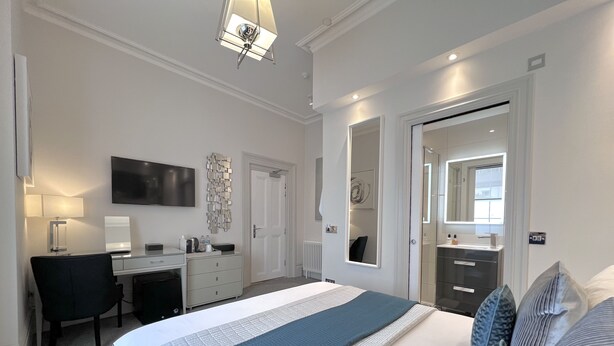 A modern bedroom with a bed, a desk, a chair, and a bathroom with a mirror. - Tavistock House Hotel (Tavistock)