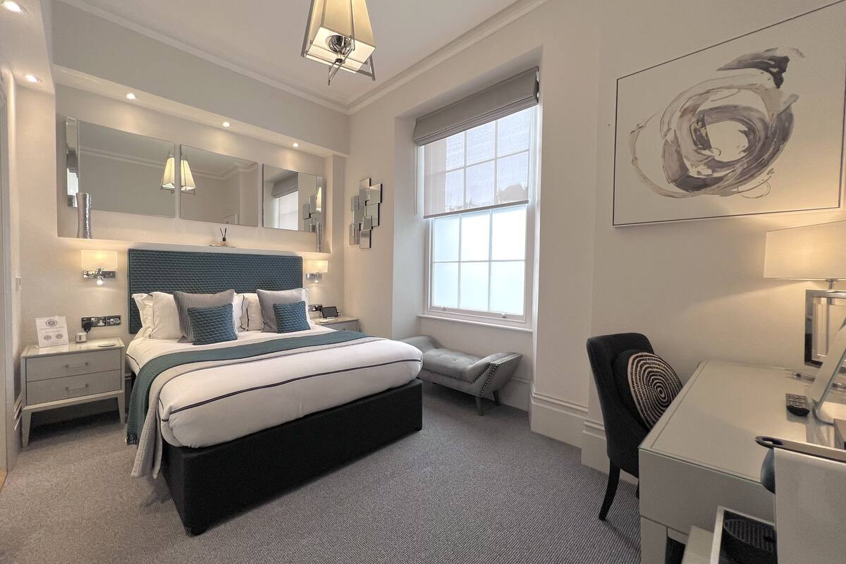 A modern hotel room with a large bed, bedside tables, a desk, and a large window.
