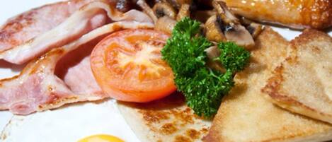 A plate of breakfast food including bacon, sausages, mushrooms, a fried egg, toast, and a tomato.